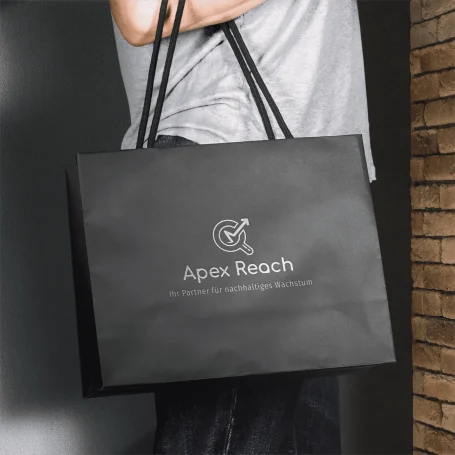 Schwarze Einkaufstasche mit dem Logo "Apex Reach" auf grauem Hintergrund.